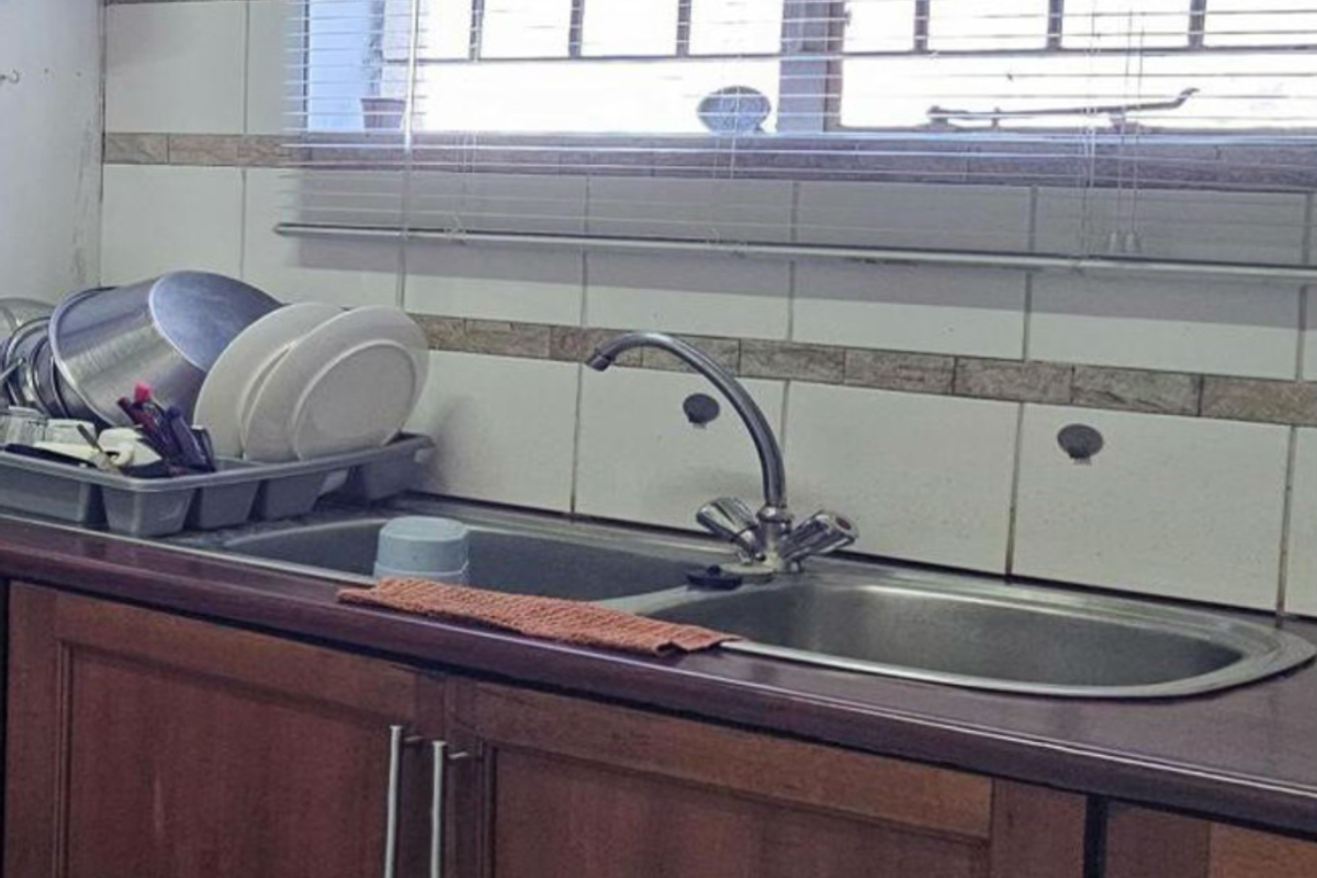 A kitchen sink area featuring timber cabinetry, tiled splashbacks, and a double bowl stainless steel sink with a mixer tap.