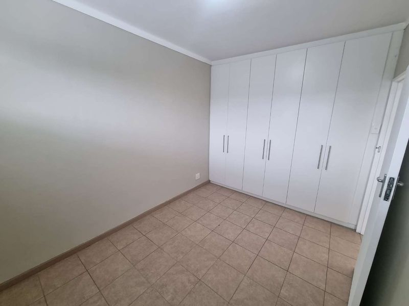 A clean, empty bedroom featuring neutral wall tones, tiled flooring, and extensive white built-in cupboards for ample storage.