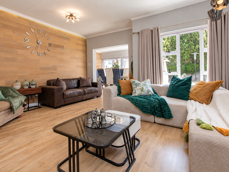 A well-appointed living room featuring a timber-clad feature wall, warm laminate flooring, and large windows that provide ample natural light.