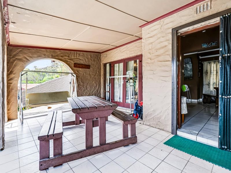 A covered outdoor patio area featuring textured stone-effect walls, tiled flooring, and an arched opening leading to the garden.