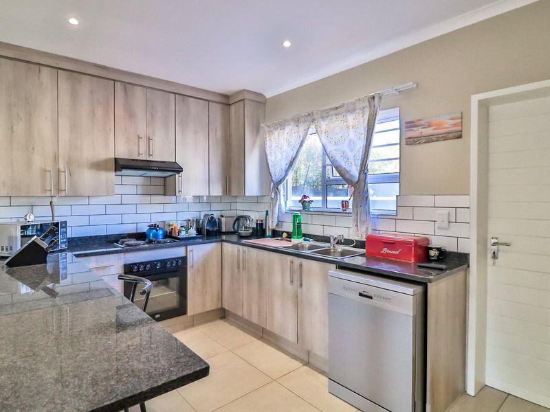 Modern kitchen featuring light wood-grain cabinetry, granite countertops, subway tile backsplash, and integrated appliances, offering a clean and functional workspace.