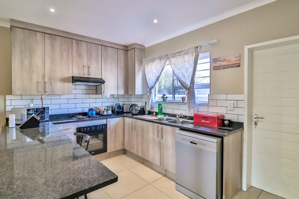 Modern kitchen featuring light wood-grain cabinetry, granite countertops, subway tile backsplash, and integrated appliances, offering a clean and functional workspace.