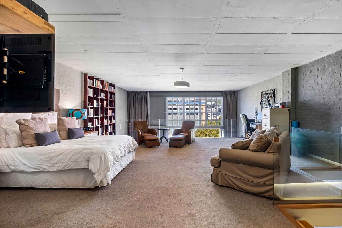 Spacious open-plan bedroom featuring an exposed concrete ceiling, built-in shelving, and a glass balustrade overlooking the lower level.
