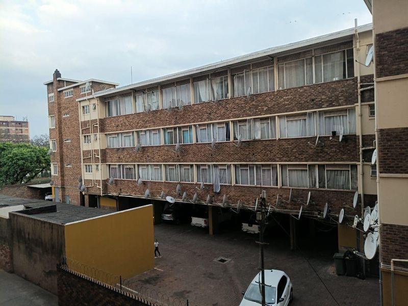 Exterior view of a multi-story brick apartment building featuring a ground-level covered parking area and numerous satellite dish installations.
