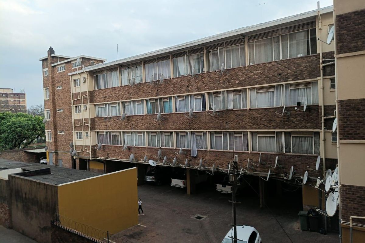 Exterior view of a multi-story brick apartment building featuring a ground-level covered parking area and numerous satellite dish installations.