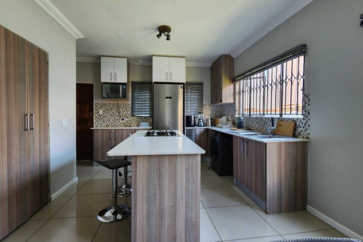 Modern kitchen featuring wood-grain cabinetry, a central island with a built-in gas hob, mosaic tile backsplash, and tiled flooring.