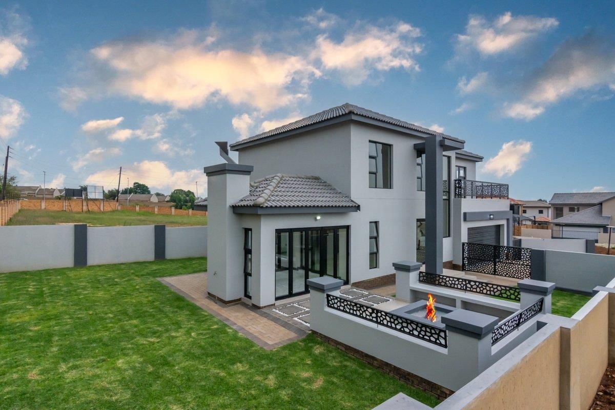 A modern two-story residential home featuring a landscaped garden, paved patio area with a built-in fire pit, and a balcony.
