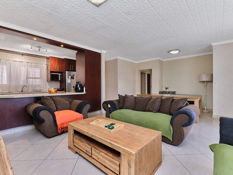 Open-plan living area featuring tiled floors, a textured ceiling, and a functional kitchen with a breakfast bar and built-in cabinetry.