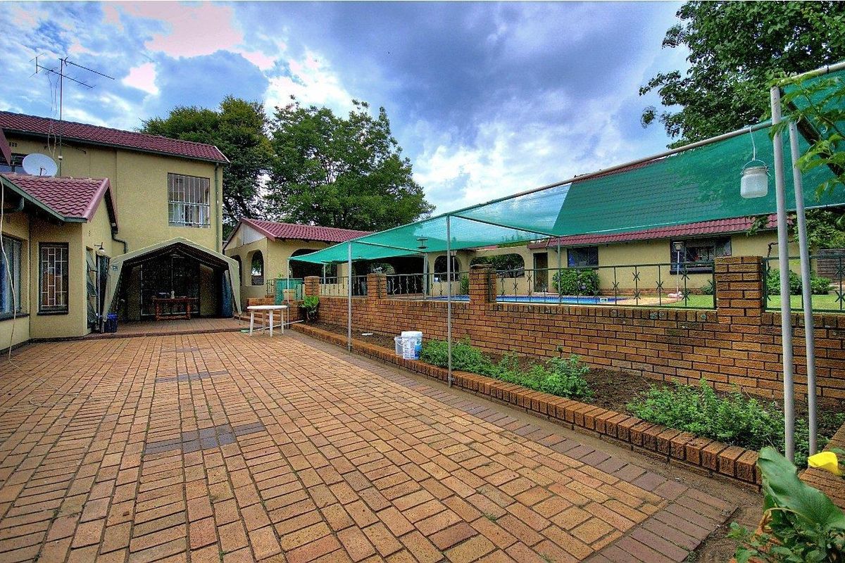 Spacious paved rear courtyard featuring a brick boundary wall, swimming pool area, and covered patio space, ideal for outdoor entertaining.