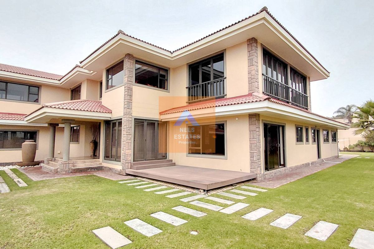 A spacious double-story residence featuring stone cladding, a tiled roof, timber decking, and a well-maintained lawn area.