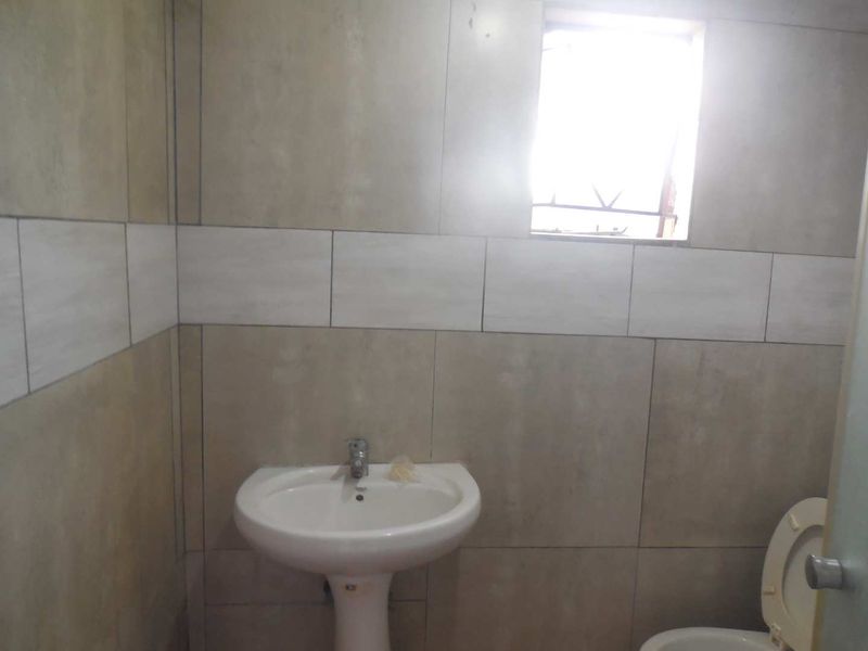 A functional bathroom featuring a pedestal basin, toilet, and neutral wall tiling with a small window for natural light.