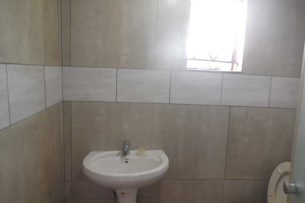 A functional bathroom featuring a pedestal basin, toilet, and neutral wall tiling with a small window for natural light.
