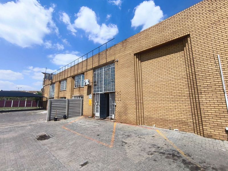 Front elevation of an industrial unit featuring face brick construction, a large roller shutter door, and paved exterior parking area.