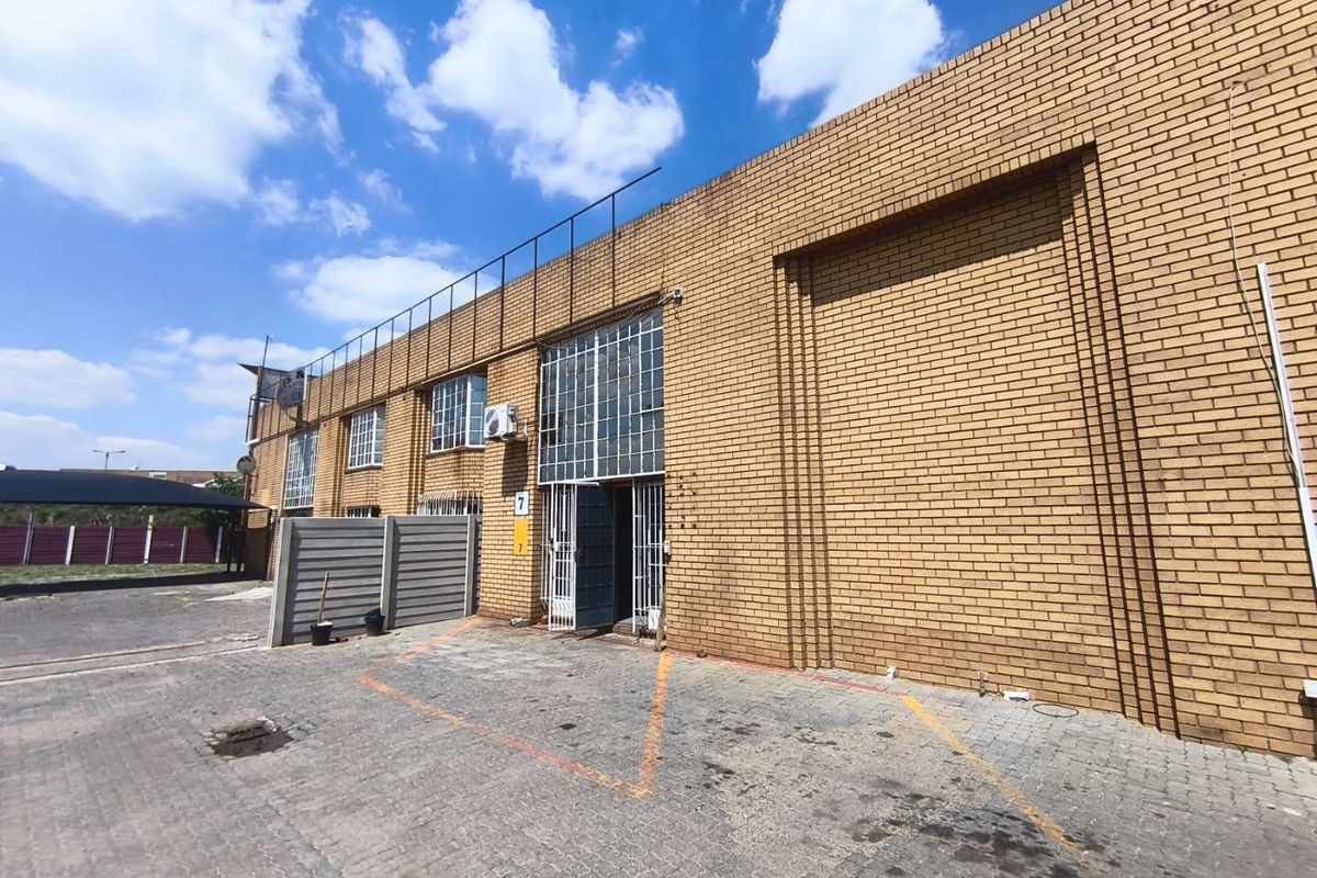 Front elevation of an industrial unit featuring face brick construction, a large roller shutter door, and paved exterior parking area.