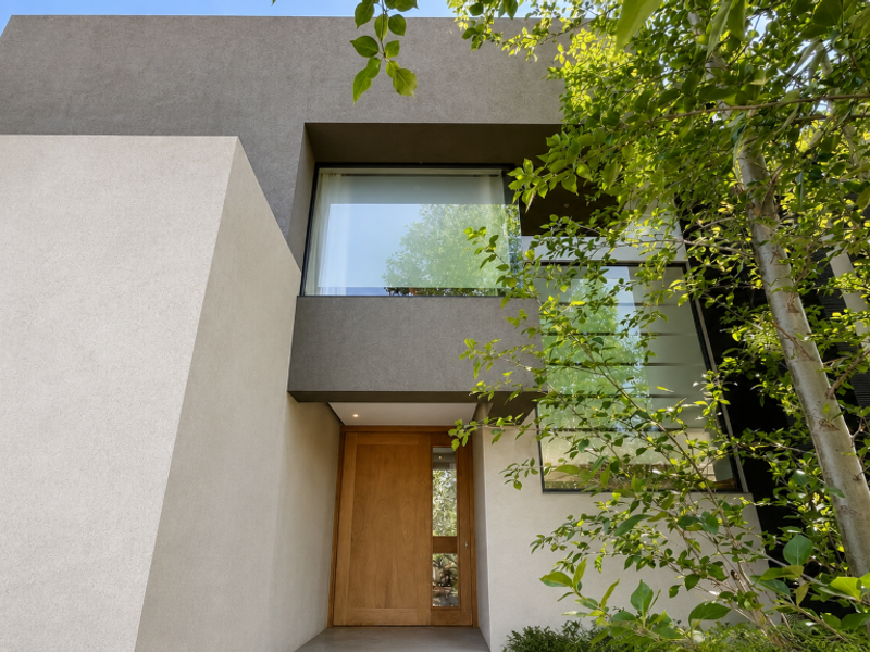 Modern architectural front facade featuring a natural timber entrance door, large glass windows, and a clean, minimalist concrete finish.