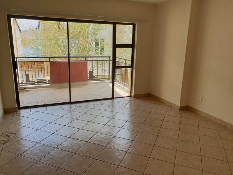 An empty living room featuring tiled flooring and large sliding glass doors that provide direct access to an outdoor balcony.