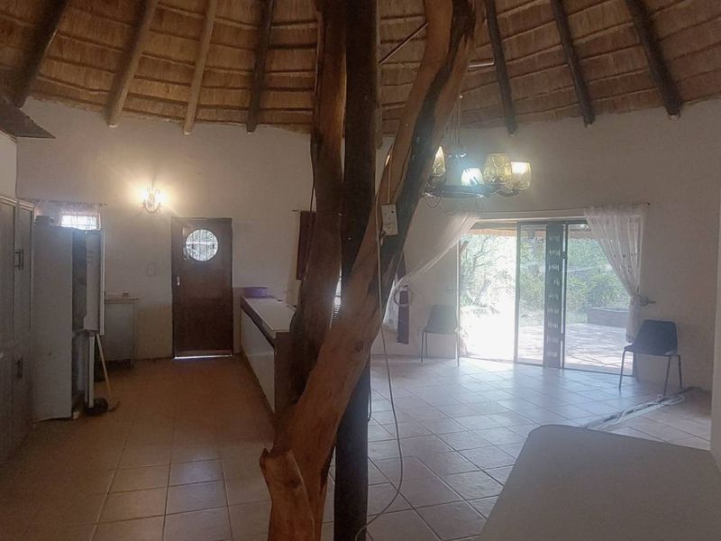 Spacious open-plan living area featuring a traditional thatched roof, exposed timber support, tiled flooring, and direct access to the outdoor patio.