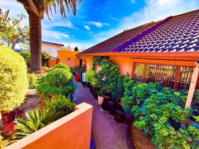 A rear exterior view of the property featuring a tiled roof, brick paved walkway, and established garden landscaping along the building facade.