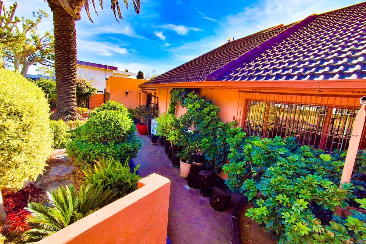 A rear exterior view of the property featuring a tiled roof, brick paved walkway, and established garden landscaping along the building facade.