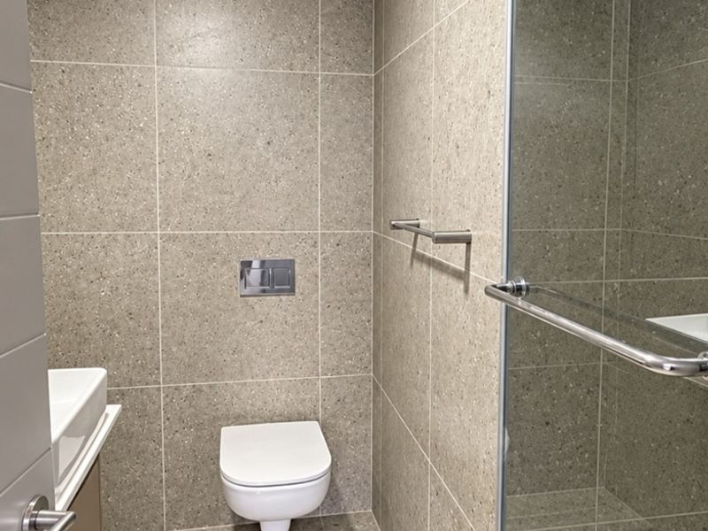 Modern bathroom featuring a wall-mounted toilet, glass shower enclosure, and neutral stone-look tiling throughout.