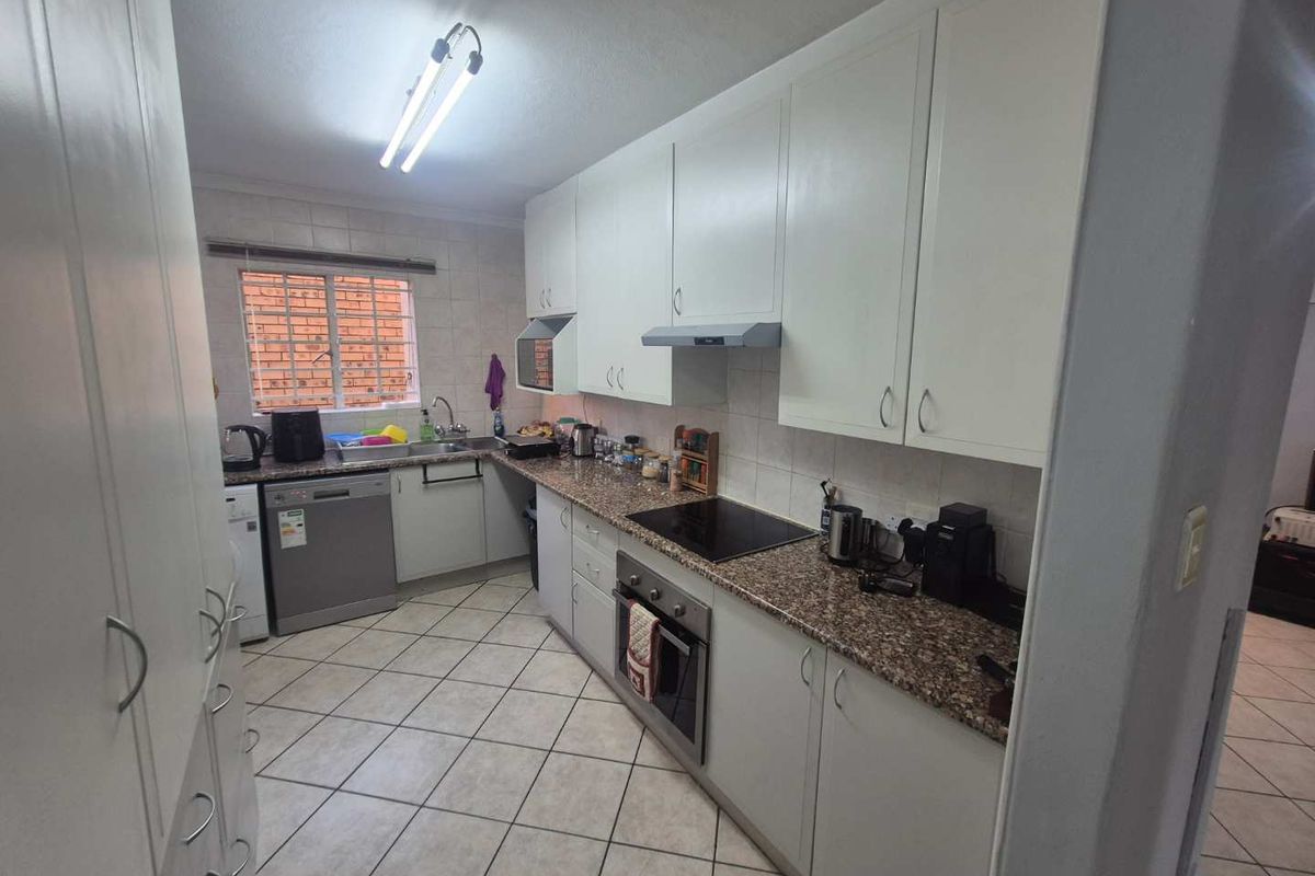 A functional galley-style kitchen featuring white cabinetry, granite-look countertops, a built-in oven, and a ceramic hob with an extractor fan.