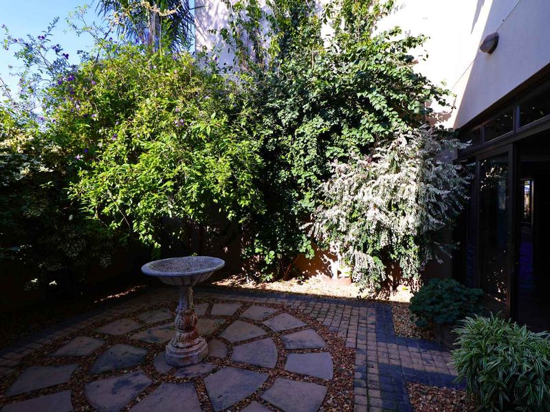 A private rear courtyard featuring a circular stone paved patio, a decorative stone bird bath, and direct access to the home via sliding glass doors.