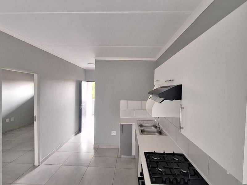 A clean, modern kitchen featuring built-in cabinetry, a gas hob with extractor fan, and a double sink, finished with neutral tiling.