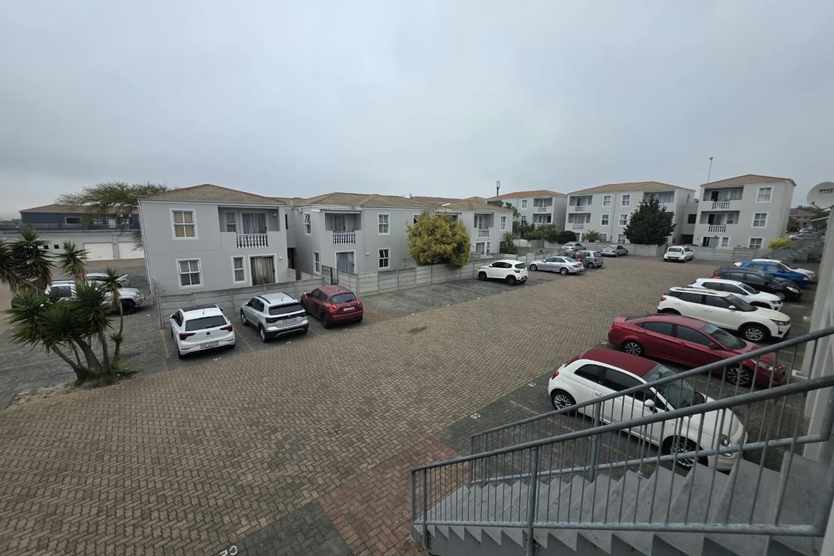 An elevated view of the apartment complex parking area, featuring paved surfaces, metal staircases, and residential building facades.
