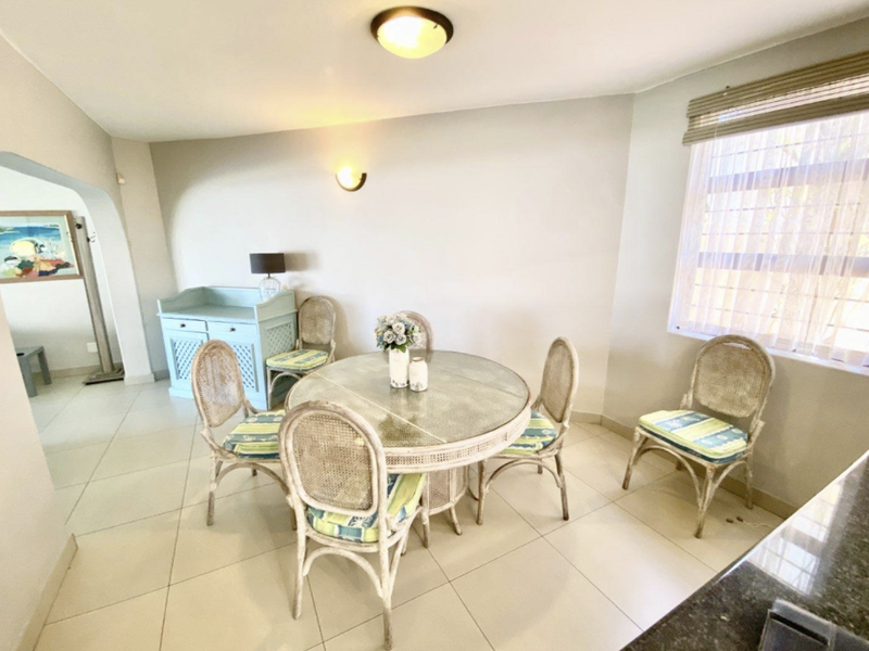A bright dining area featuring neutral tiled flooring, a classic archway entrance, and natural light provided by a window with fitted blinds.