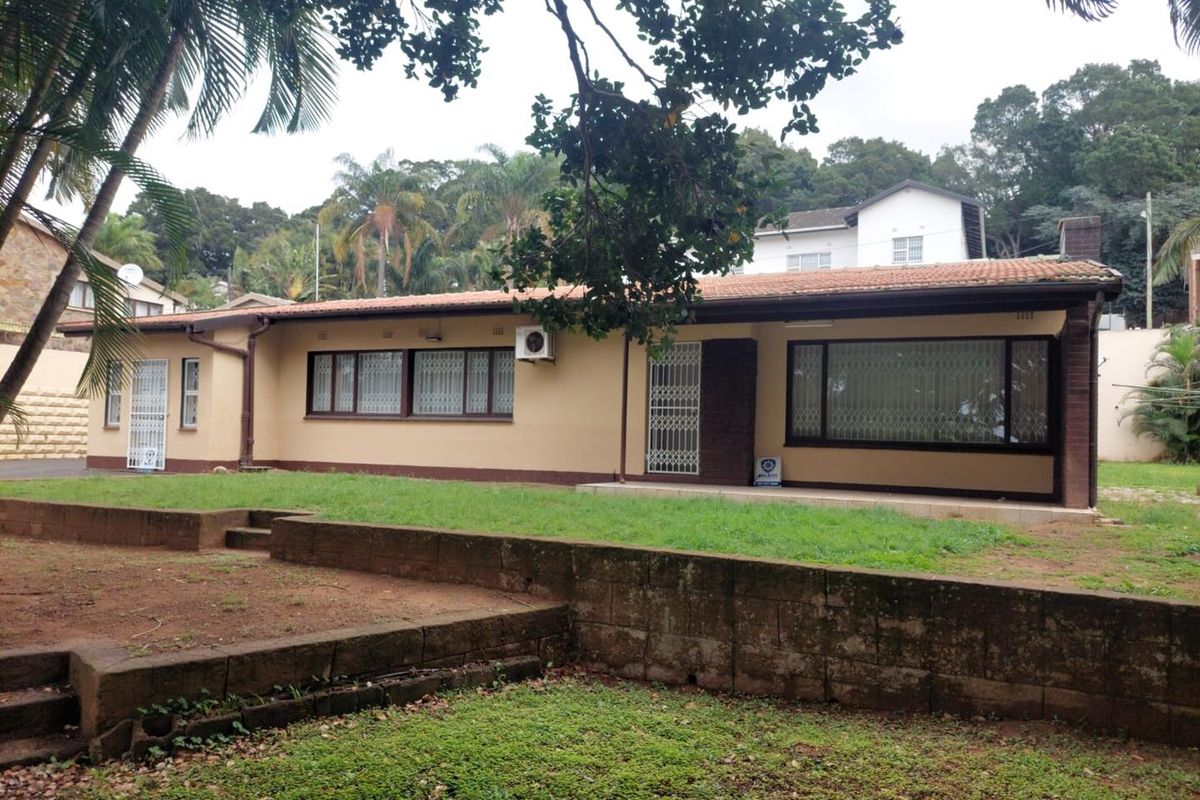 Rear view of a single-story house featuring a terracotta tile roof, security gates, and a concrete patio area overlooking a tiered garden.