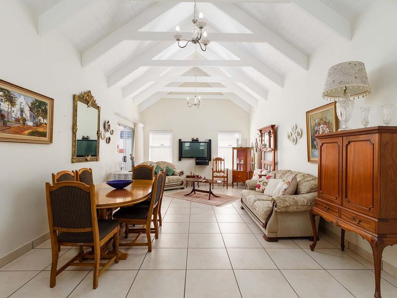 Spacious open-plan living and dining area featuring a high vaulted ceiling with exposed beams, ceramic tiled flooring, and abundant natural light.