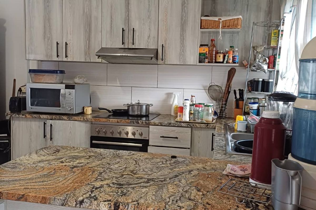 A functional kitchen featuring wood-look laminate cabinetry, a striking stone countertop, built-in oven, extractor fan, and a tiled backsplash.