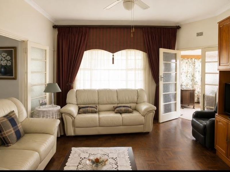 A traditional living room featuring warm parquet flooring, crown molding, a ceiling fan, and classic French doors leading to adjacent spaces.