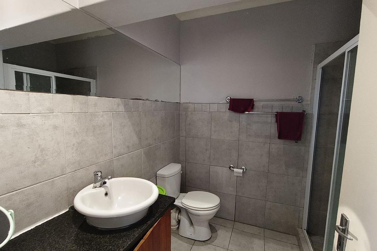 A functional bathroom featuring a vanity with granite countertop, ceramic basin, toilet, and a glass-enclosed shower with neutral wall and floor tiling.