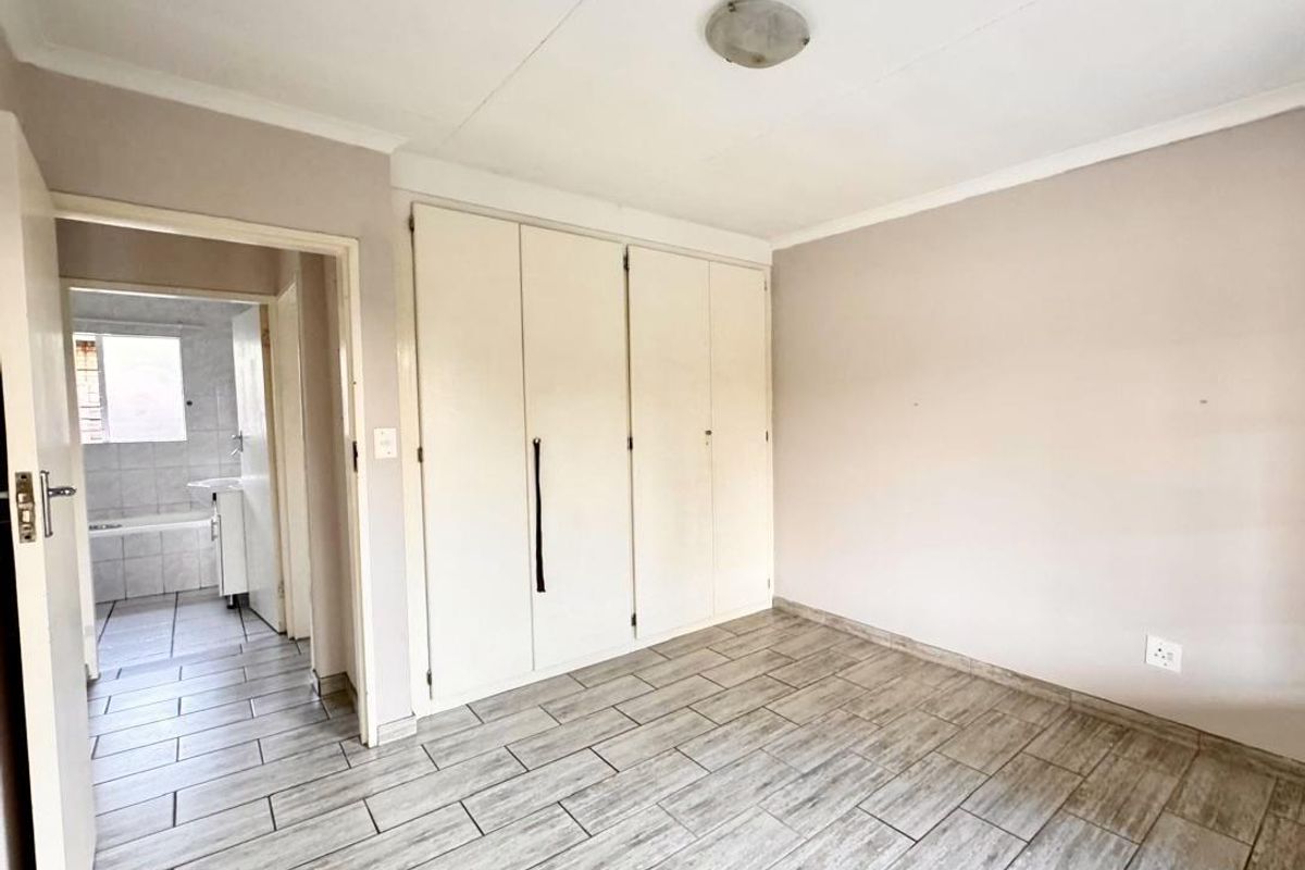 A clean, empty bedroom featuring tiled flooring, built-in cupboards, and direct access to an adjoining bathroom.