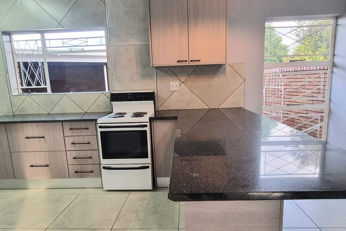 A functional kitchen featuring light wood cabinetry, dark granite countertops, a freestanding stove, and tiled flooring with a breakfast bar area.