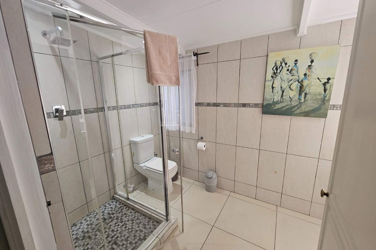 A clean, functional bathroom featuring a glass-enclosed shower with mosaic tile flooring, a standard toilet, and neutral wall tiling throughout.