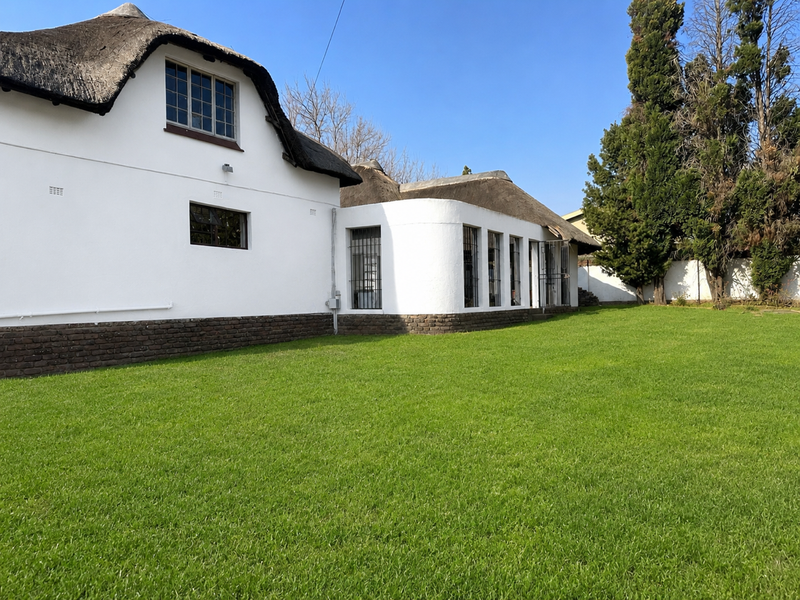 Rear view of a white-walled house featuring a traditional thatch roof, brick base, and a well-maintained green lawn.