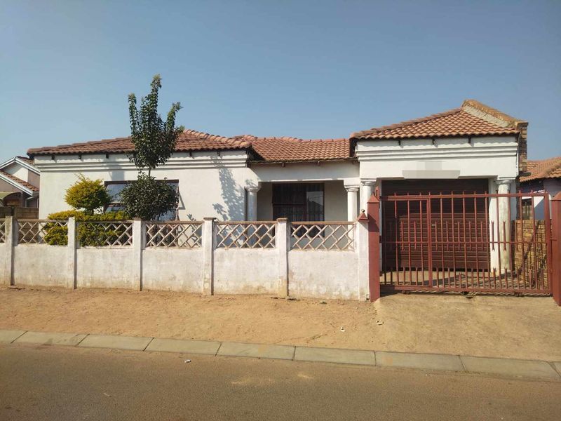 Front elevation of a single-story house featuring a tiled roof, perimeter wall with lattice detailing, and a secure metal driveway gate.