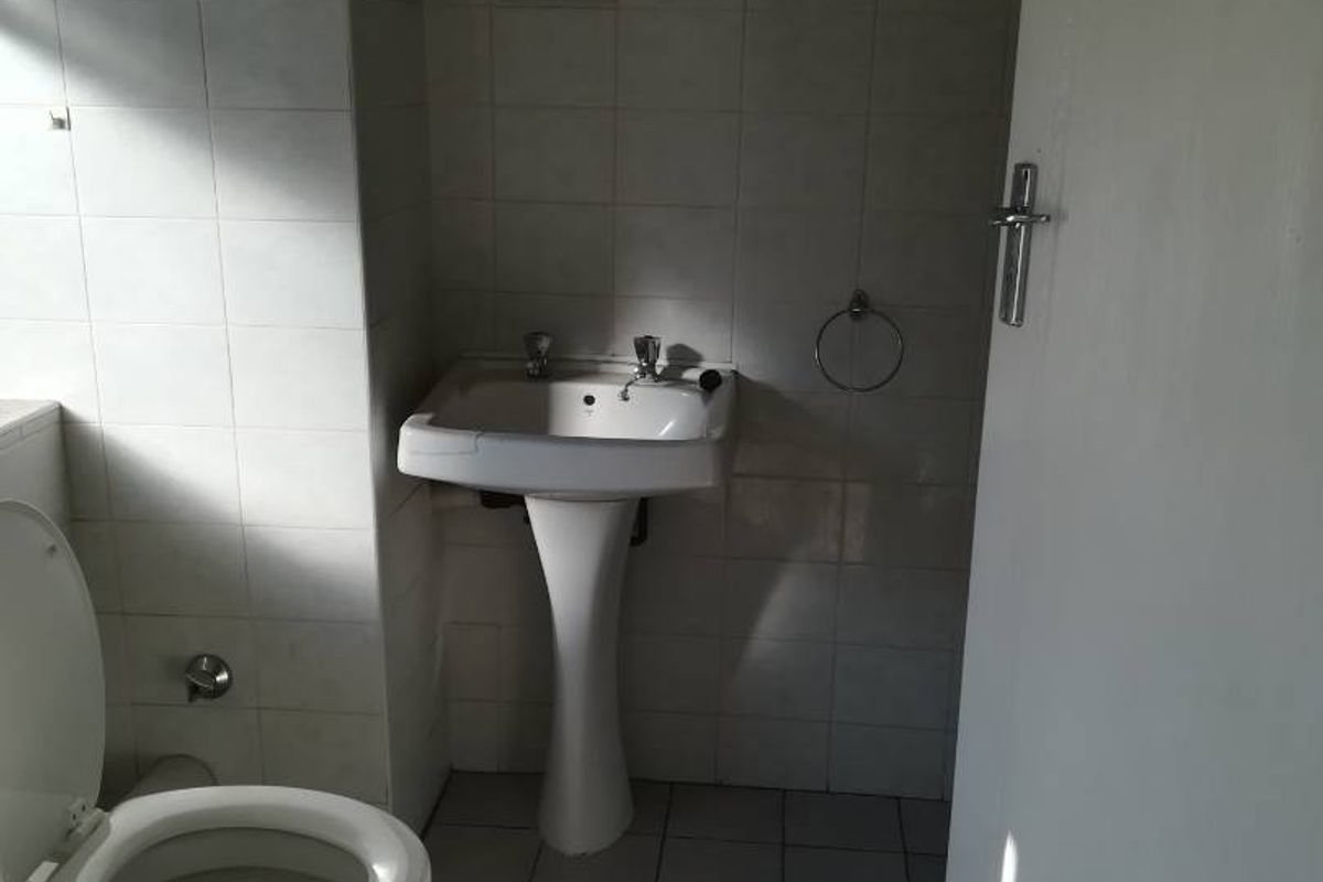 A functional bathroom featuring a pedestal basin, toilet, and neutral tiled finishes, offering a clean and simple layout.