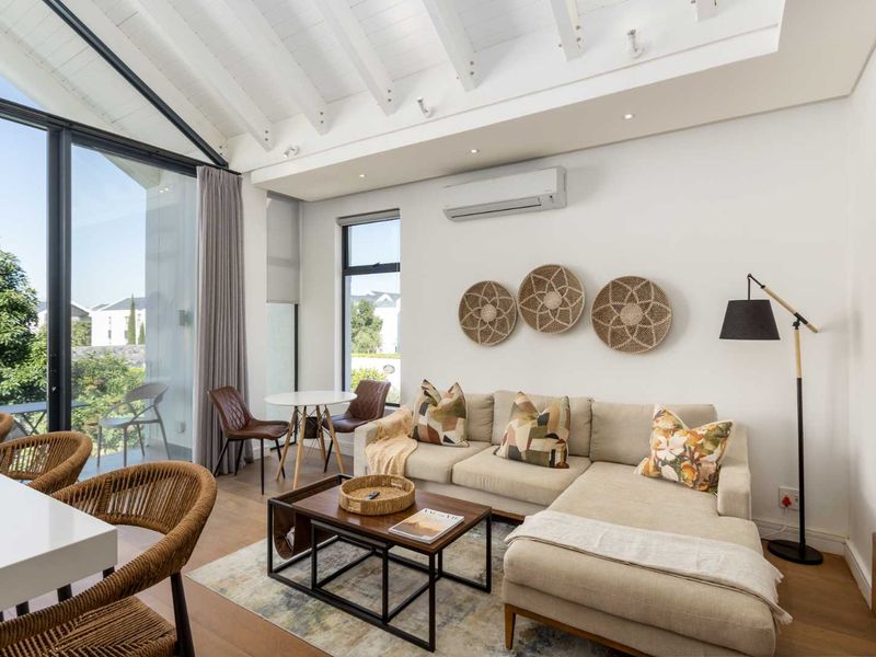 Bright and modern living area featuring vaulted ceilings with exposed beams, timber flooring, and large glass doors opening to an outdoor patio.