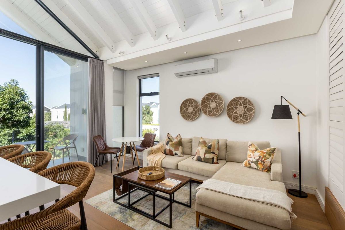 Bright and modern living area featuring vaulted ceilings with exposed beams, timber flooring, and large glass doors opening to an outdoor patio.