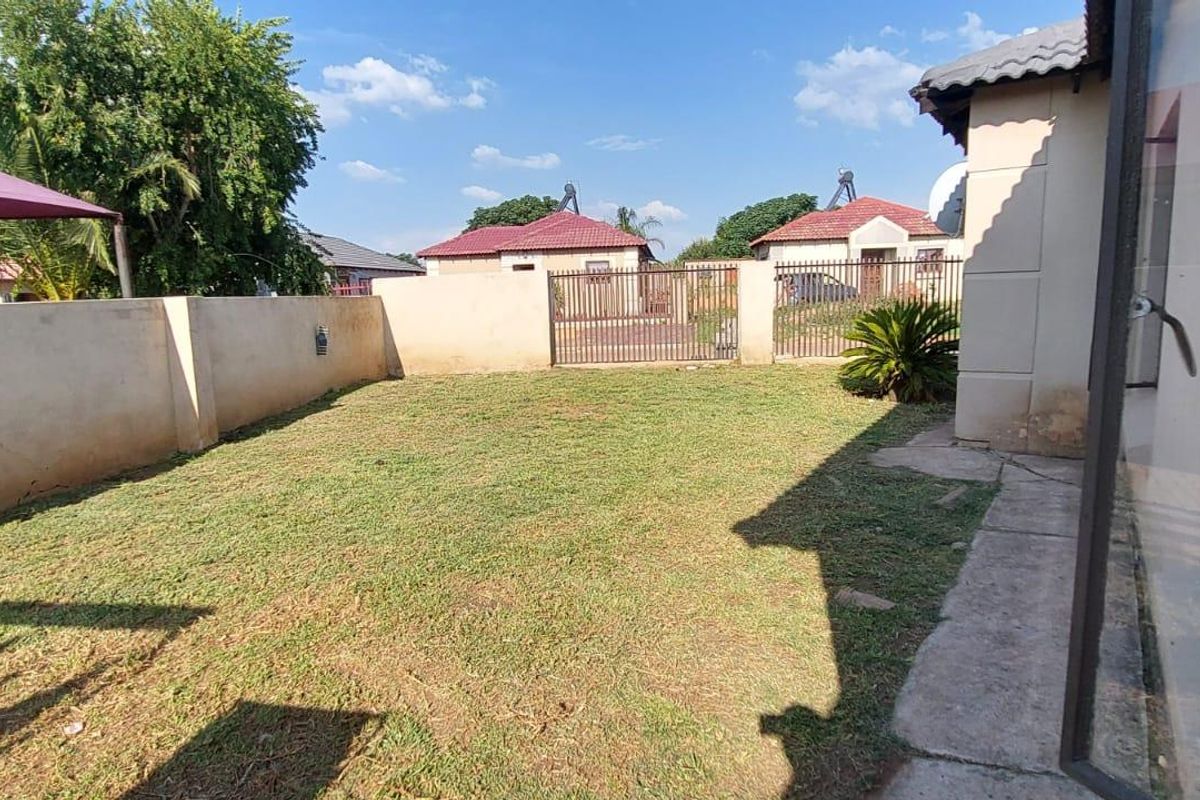 A private rear garden area featuring a lawn, perimeter boundary walls, and a metal access gate.