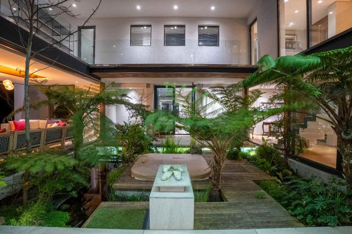 A beautifully landscaped central courtyard featuring a built-in spa, timber decking, and lush greenery, surrounded by modern architectural glass walls.