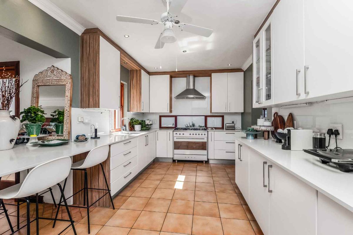 A well-maintained kitchen featuring white cabinetry, stone countertops, a freestanding gas stove, stainless steel extractor fan, and tiled flooring.