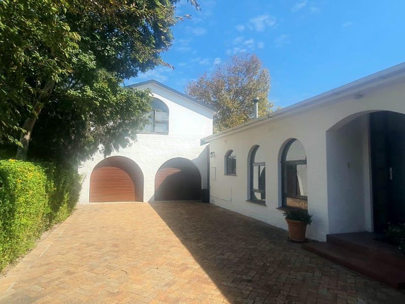 Front exterior view featuring a paved driveway, double garage with arched doors, and a white facade with arched windows and entrance.