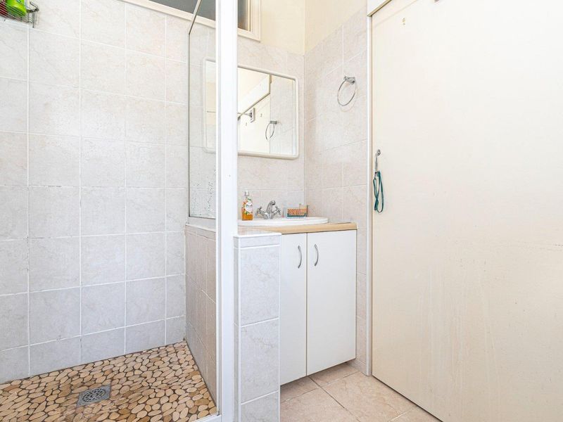 A functional bathroom featuring a shower enclosure with a pebble-tiled floor, a vanity cabinet with a basin, and neutral wall tiling.