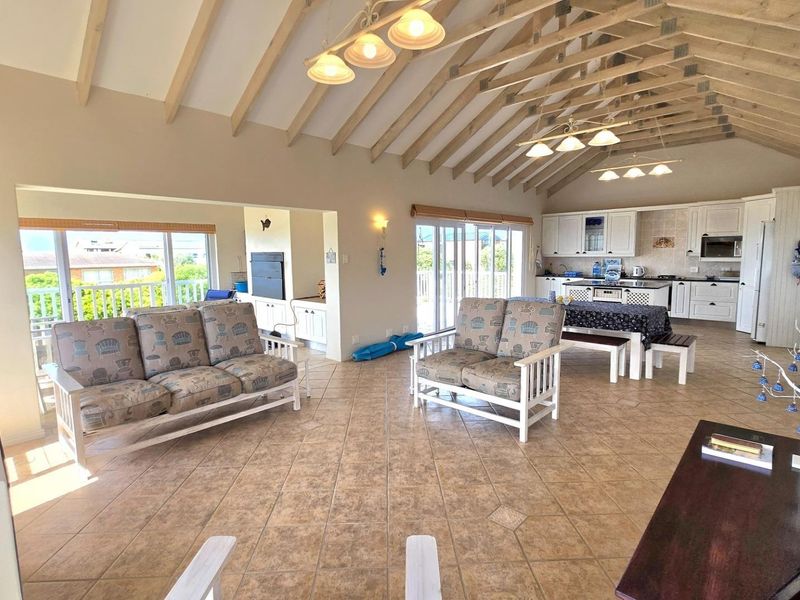 Spacious open-plan living and kitchen area featuring a high vaulted timber ceiling, tiled floors, and direct access to a balcony through sliding glass doors.