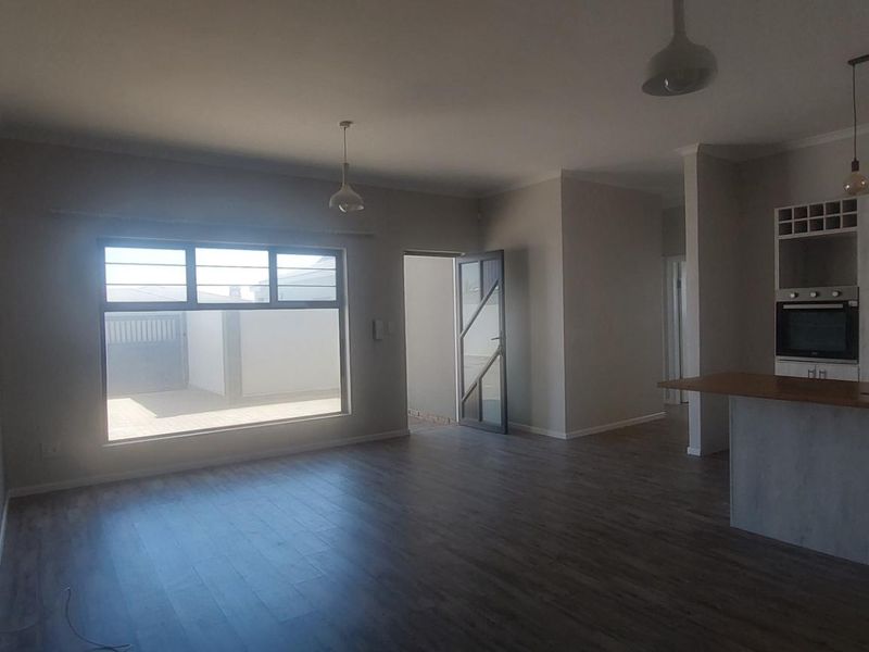 Spacious open-plan living and kitchen area featuring modern laminate flooring, built-in cabinetry, and a functional kitchen island with integrated oven.