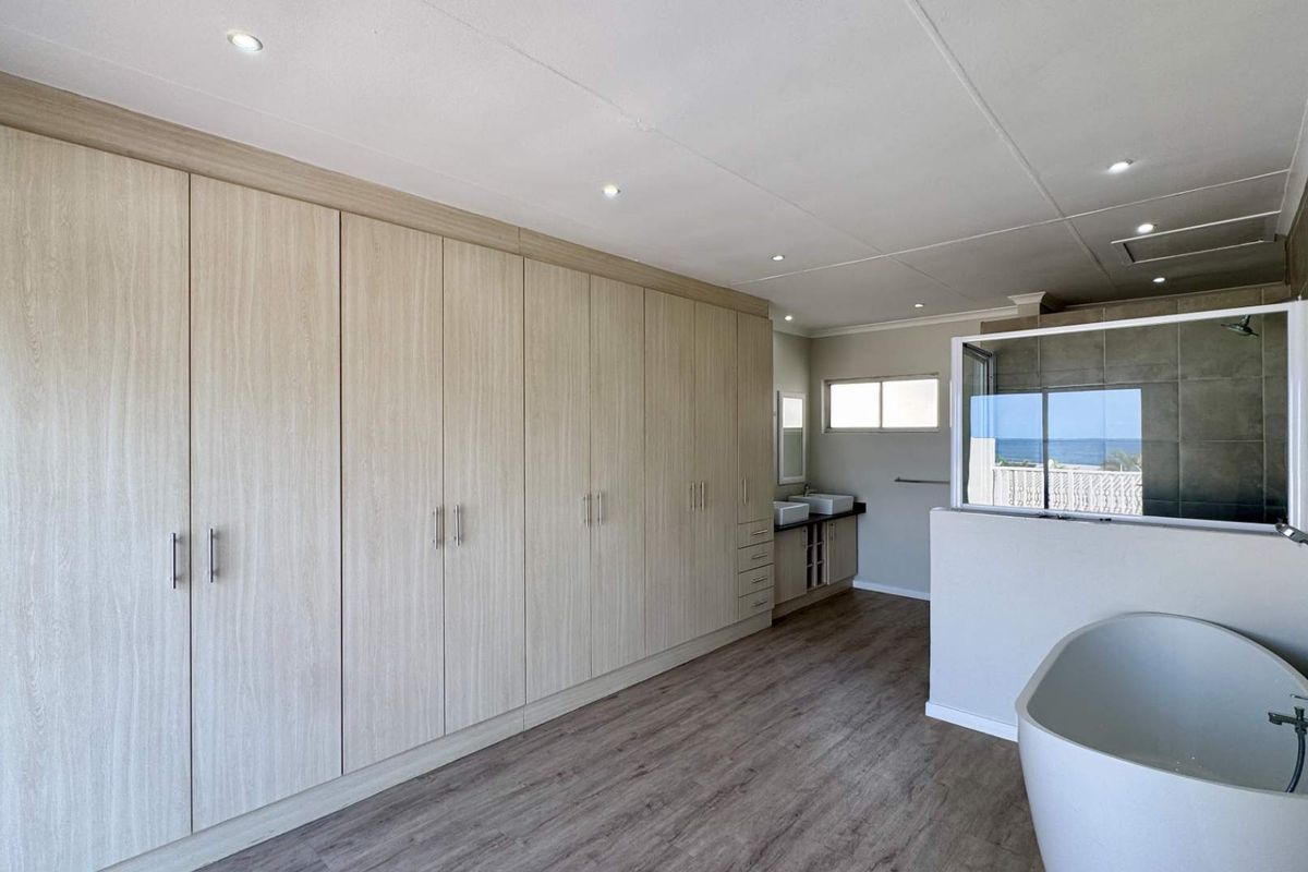 Spacious modern bathroom featuring extensive built-in cabinetry, a freestanding bathtub, double vanity, and a glass-enclosed shower with ocean views.